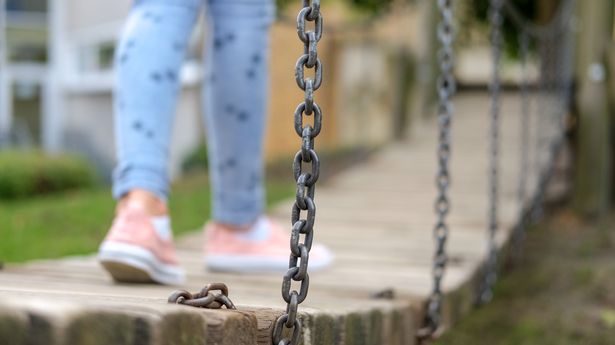 Young, slim girl is balancing on a jungle bridge in a playground / selective focus, lots of copy space