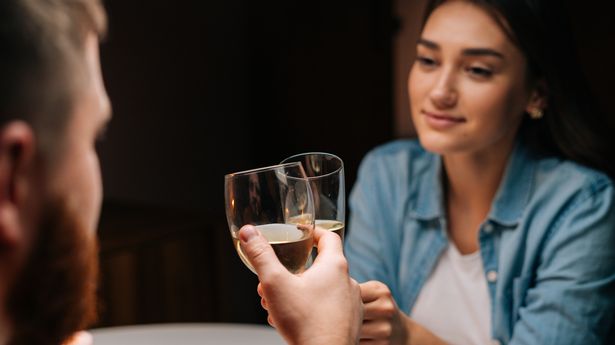 Close-up back view of happy young couple clinking glasses with champagne at table in cozy dark restaurant. Loving man and woman celebrating anniversary, Valentines day, enjoying romantic date.