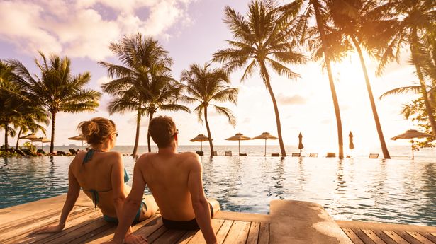 Couple enjoying beach vacation holidays at tropical resort with swimming pool and coconut palm trees near the coast with beautiful landscape at sunset, honeymoon destination